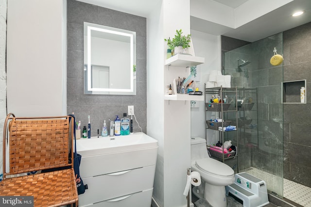 full bath featuring toilet, vanity, a walk in shower, and tile walls