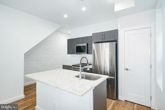 kitchen with light wood-style flooring, a kitchen island with sink, appliances with stainless steel finishes, and gray cabinetry