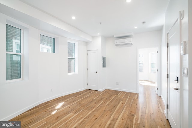 spare room with recessed lighting, a wall unit AC, light wood-style floors, electric panel, and baseboards