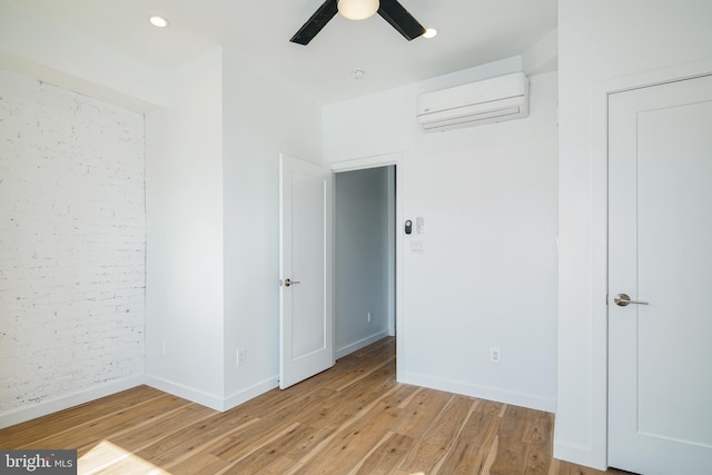 unfurnished bedroom featuring a wall mounted air conditioner, light wood finished floors, baseboards, and a ceiling fan