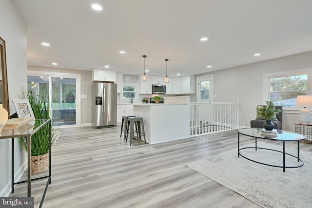 kitchen with appliances with stainless steel finishes, light wood-type flooring, a kitchen bar, pendant lighting, and white cabinets