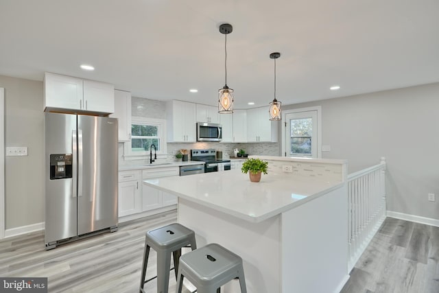 kitchen with white cabinetry, stainless steel appliances, light hardwood / wood-style flooring, and a kitchen bar