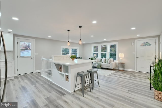 kitchen with decorative backsplash, a kitchen breakfast bar, pendant lighting, light wood-type flooring, and white cabinets