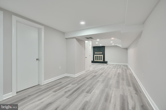 basement with light wood-type flooring and a brick fireplace