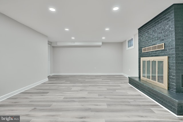 basement featuring a wealth of natural light, light wood-type flooring, and a brick fireplace