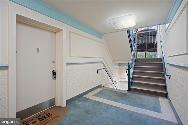 staircase with brick wall and carpet floors