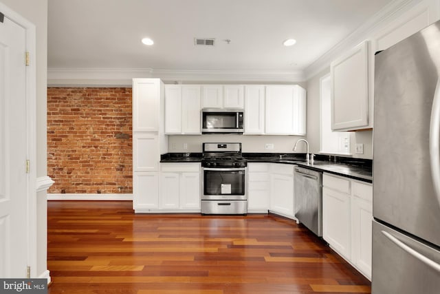 kitchen with dark wood-type flooring, stainless steel appliances, sink, and brick wall