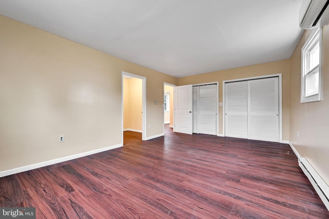 unfurnished bedroom featuring dark hardwood / wood-style floors, baseboard heating, a wall unit AC, and multiple closets