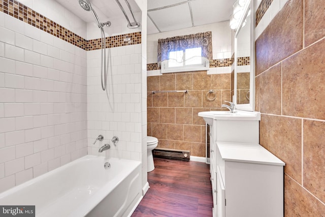 full bathroom featuring vanity, a baseboard heating unit, tiled shower / bath combo, tile walls, and wood-type flooring