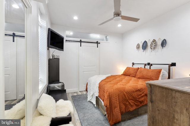 bedroom featuring ceiling fan, a barn door, and light hardwood / wood-style floors