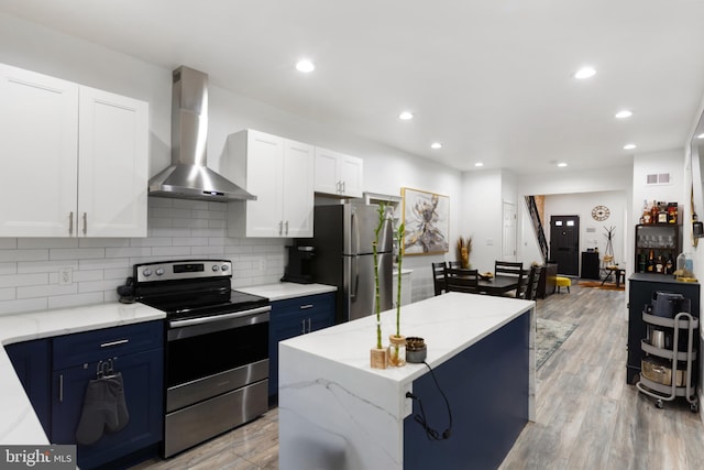 kitchen featuring blue cabinetry, wall chimney exhaust hood, a kitchen island, white cabinets, and appliances with stainless steel finishes