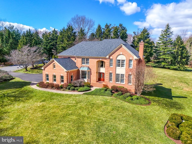 colonial inspired home with a shingled roof, a front yard, brick siding, and a chimney