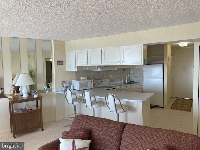 kitchen with kitchen peninsula, backsplash, white cabinetry, sink, and white appliances