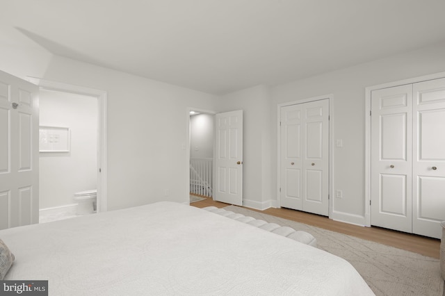 bedroom featuring light wood-type flooring, two closets, and connected bathroom