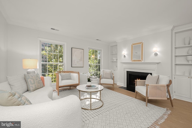 living room with built in shelves, light wood-type flooring, and ornamental molding