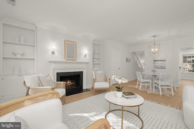 living room featuring an inviting chandelier, built in features, light hardwood / wood-style floors, and ornamental molding