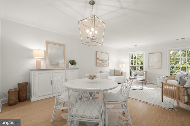 dining area with a notable chandelier, light wood-type flooring, and crown molding