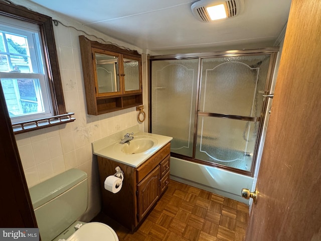 full bathroom with tile walls, vanity, parquet flooring, shower / bath combination with glass door, and toilet