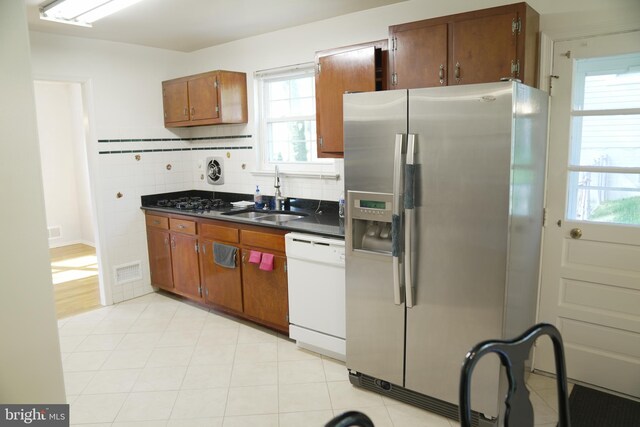 kitchen featuring a healthy amount of sunlight, backsplash, stainless steel fridge with ice dispenser, white dishwasher, and sink