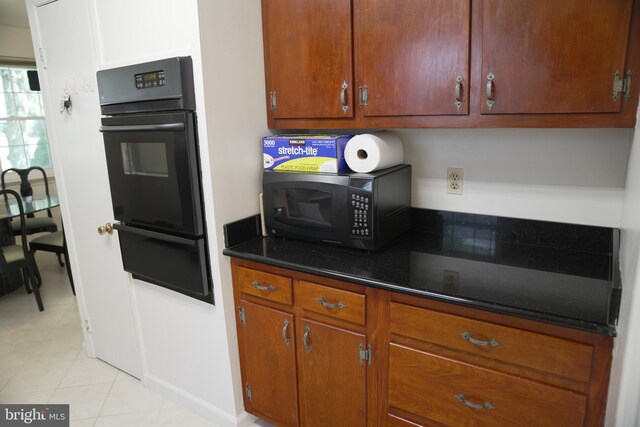 kitchen featuring black appliances, light tile patterned floors, and dark stone countertops