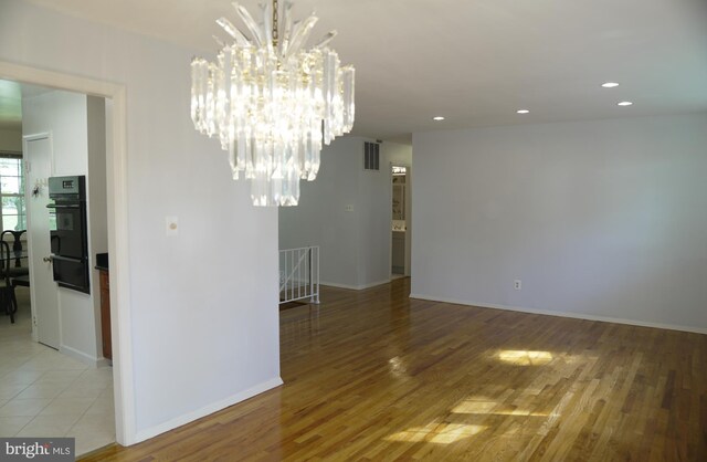 empty room with light hardwood / wood-style flooring and a notable chandelier