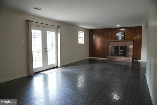 unfurnished living room featuring french doors, wooden walls, and a fireplace