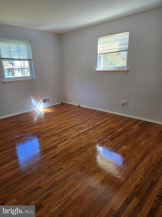 empty room with a wealth of natural light and dark hardwood / wood-style flooring