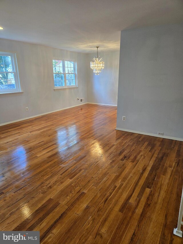 empty room with a notable chandelier, a wealth of natural light, and dark hardwood / wood-style floors