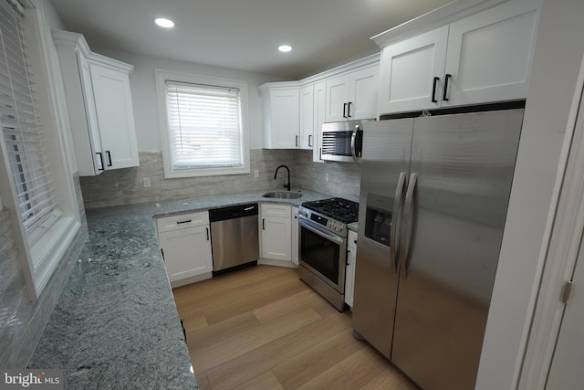 kitchen with light stone counters, white cabinets, sink, stainless steel appliances, and light hardwood / wood-style floors