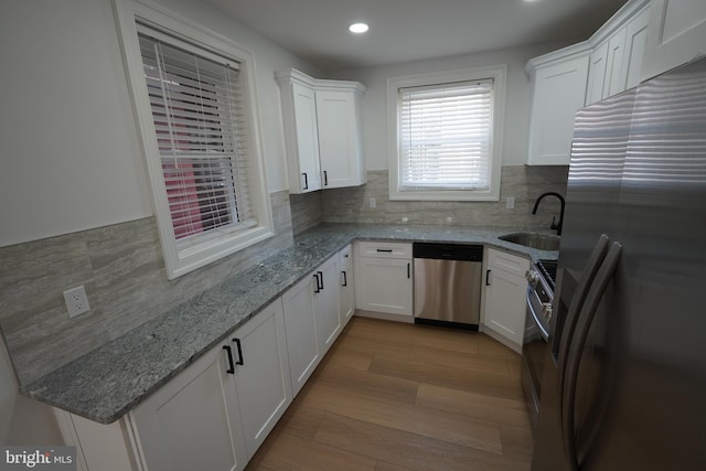 kitchen with light wood-type flooring, sink, white cabinets, decorative backsplash, and stainless steel appliances