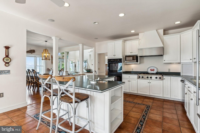 kitchen featuring ornate columns, decorative light fixtures, stainless steel appliances, white cabinets, and custom exhaust hood