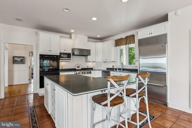 kitchen featuring premium range hood, built in appliances, tile patterned flooring, and white cabinets