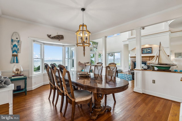 dining room with a water view, wood-type flooring, crown molding, and decorative columns