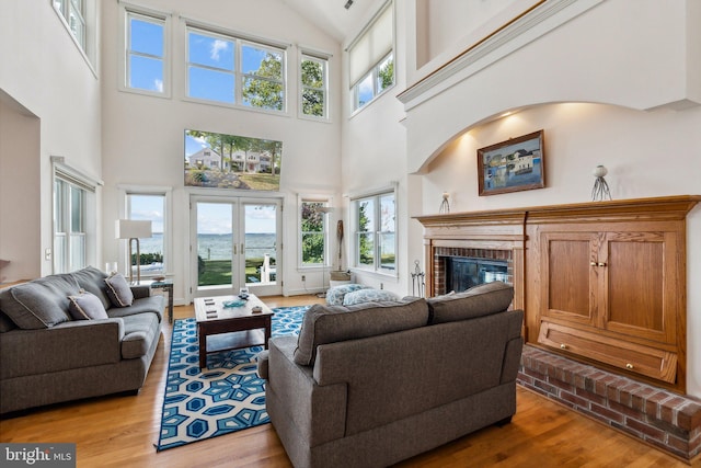 living room featuring french doors, a brick fireplace, light hardwood / wood-style floors, and a high ceiling