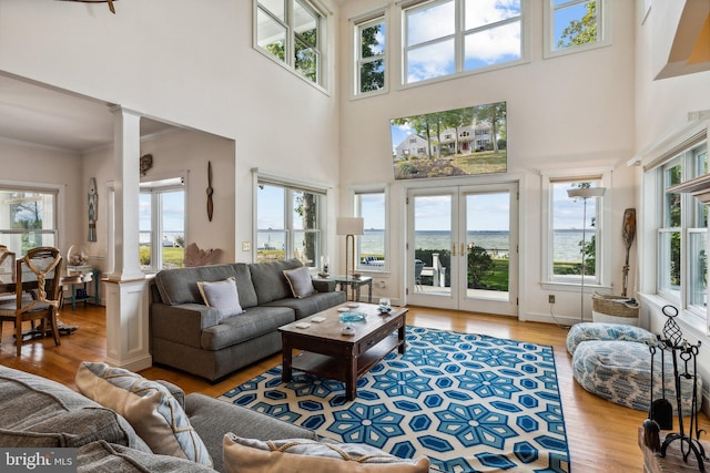 living room featuring ornate columns, french doors, light hardwood / wood-style floors, and a high ceiling