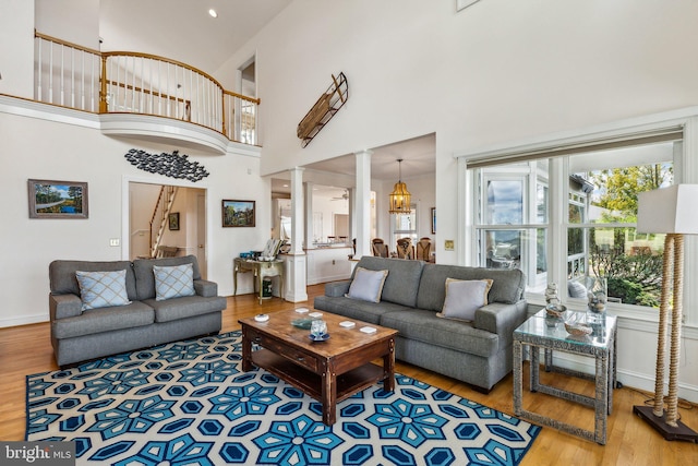 living room featuring a towering ceiling, decorative columns, a chandelier, and hardwood / wood-style flooring