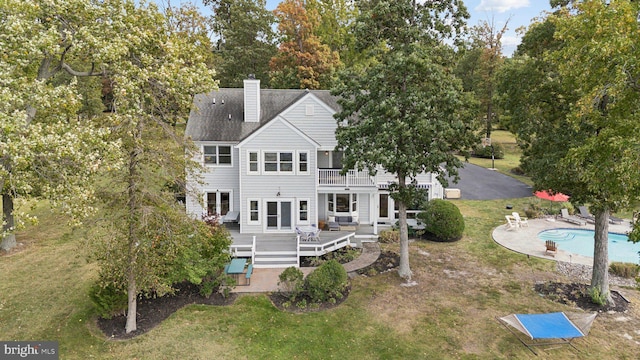 rear view of property featuring a pool side deck, a balcony, a lawn, and a patio area