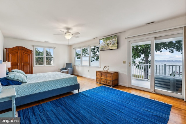 bedroom with access to exterior, ceiling fan, a water view, and hardwood / wood-style flooring