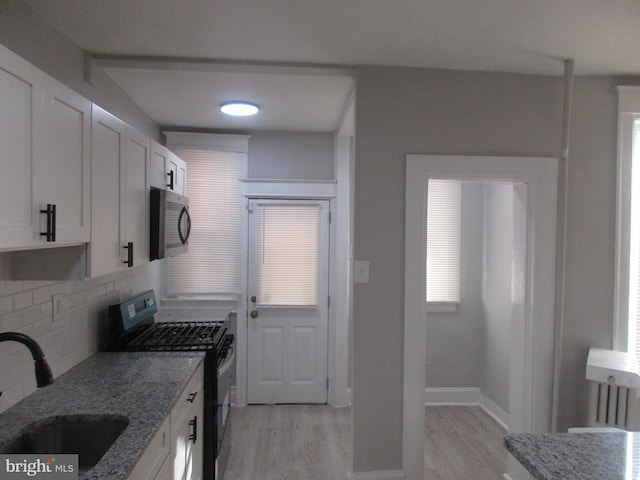 kitchen featuring black range, light stone countertops, sink, and white cabinets