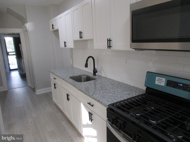 kitchen featuring appliances with stainless steel finishes, white cabinetry, light stone counters, light hardwood / wood-style flooring, and sink