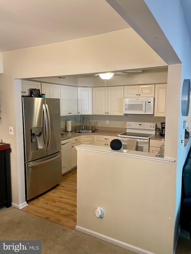 kitchen with white appliances, white cabinetry, sink, and light wood-type flooring