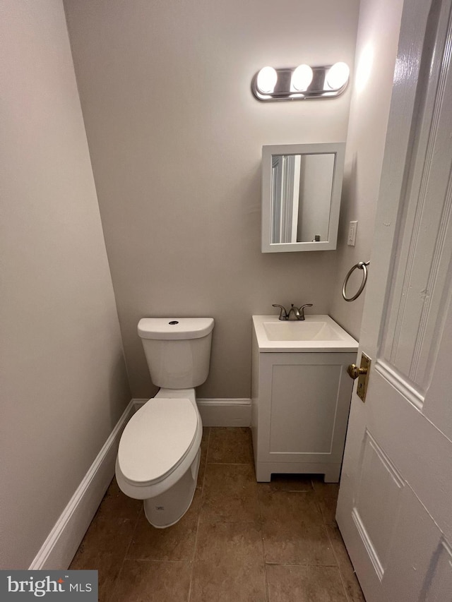 half bath featuring tile patterned floors, vanity, baseboards, and toilet
