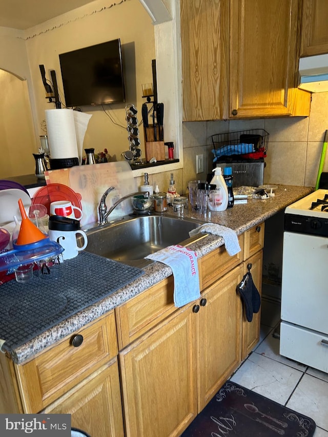 kitchen featuring white stove, dark tile patterned flooring, light stone counters, sink, and decorative backsplash