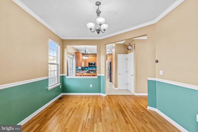 unfurnished dining area featuring a notable chandelier, ornamental molding, and light wood-type flooring