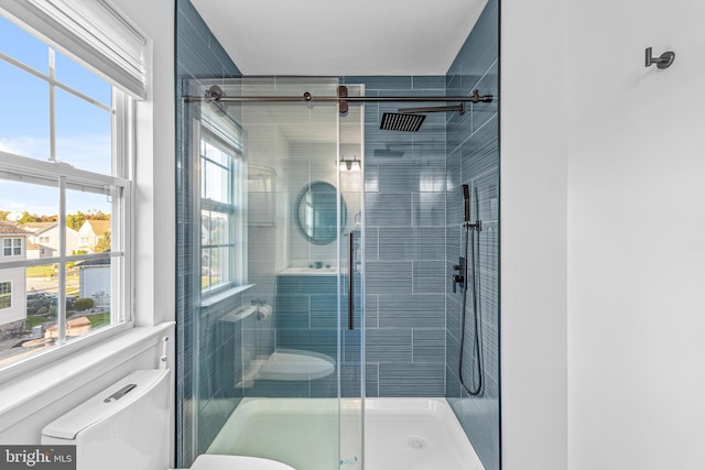 bathroom featuring a shower with door, toilet, and a healthy amount of sunlight