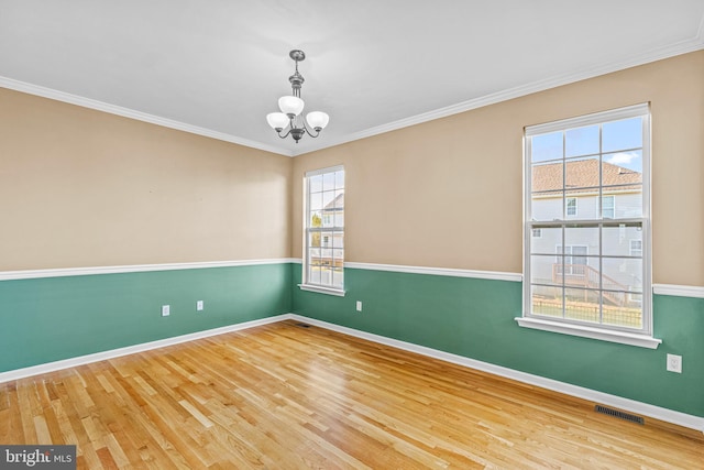 spare room with an inviting chandelier, hardwood / wood-style flooring, and crown molding