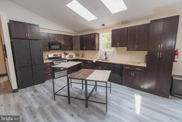 kitchen featuring vaulted ceiling with skylight, light hardwood / wood-style flooring, decorative light fixtures, sink, and black appliances