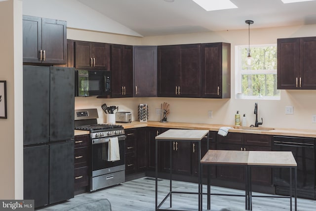 kitchen with black appliances, sink, light hardwood / wood-style floors, lofted ceiling with skylight, and decorative light fixtures