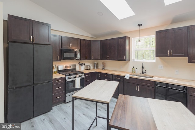 kitchen featuring vaulted ceiling with skylight, light hardwood / wood-style floors, gas stove, decorative light fixtures, and sink