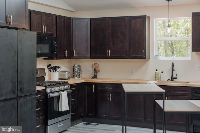 kitchen featuring dark brown cabinetry, refrigerator, stainless steel range with gas stovetop, sink, and decorative light fixtures